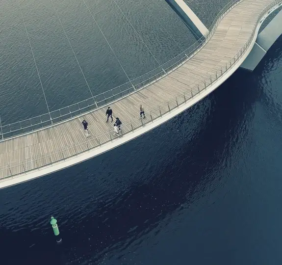 People walking on a winding bridge over water.